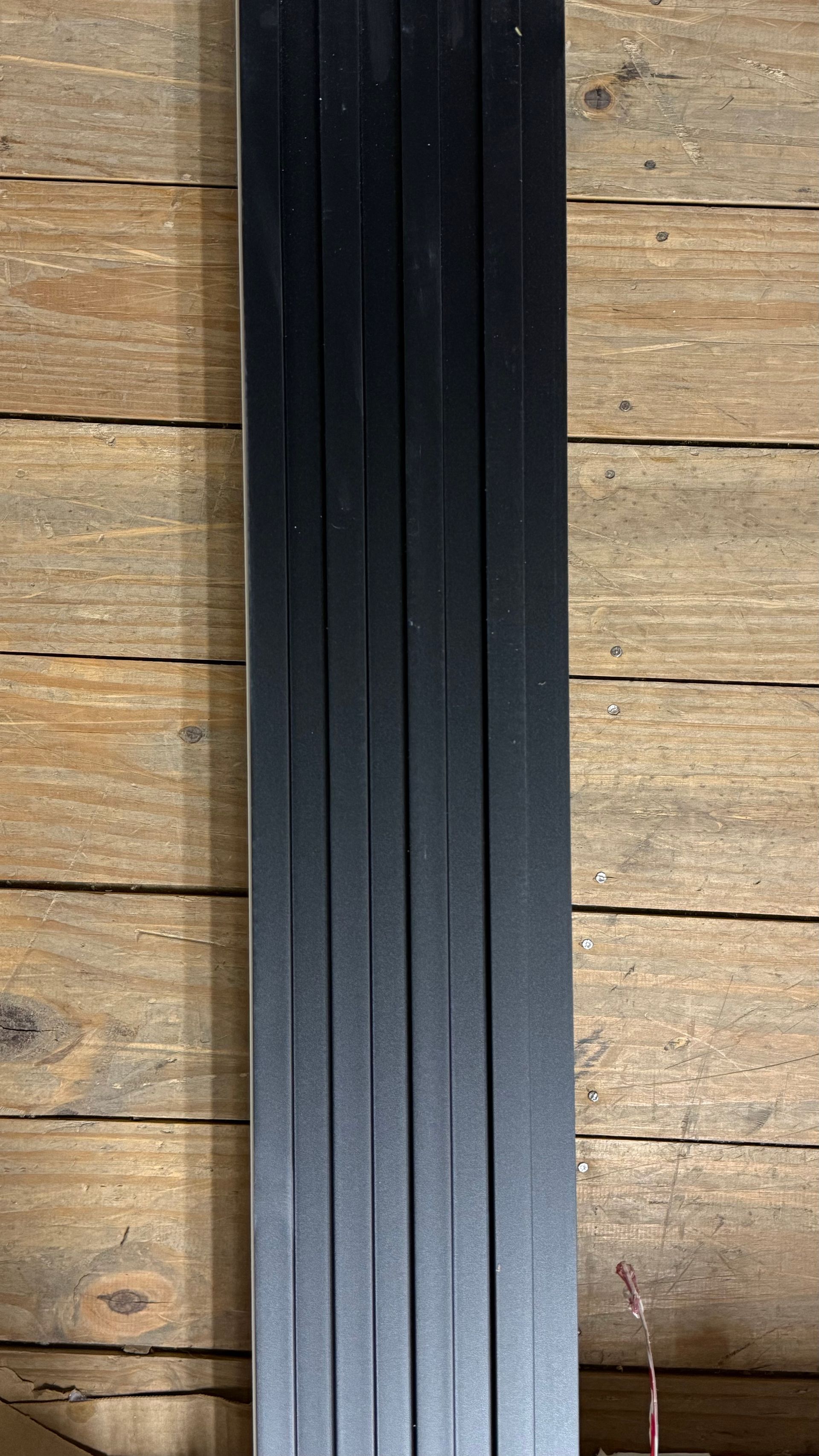 Panel vertical de listones negros sobre un fondo de suelo de madera rústica.