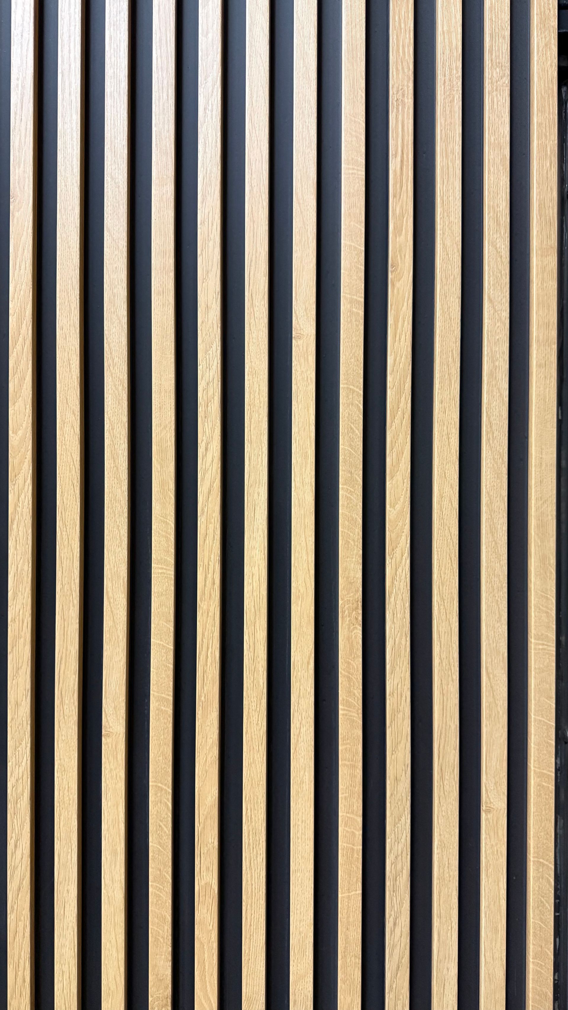 Panel vertical de listones de madera sobre un suelo de madera oscura, con franjas alternas de madera clara y negro.