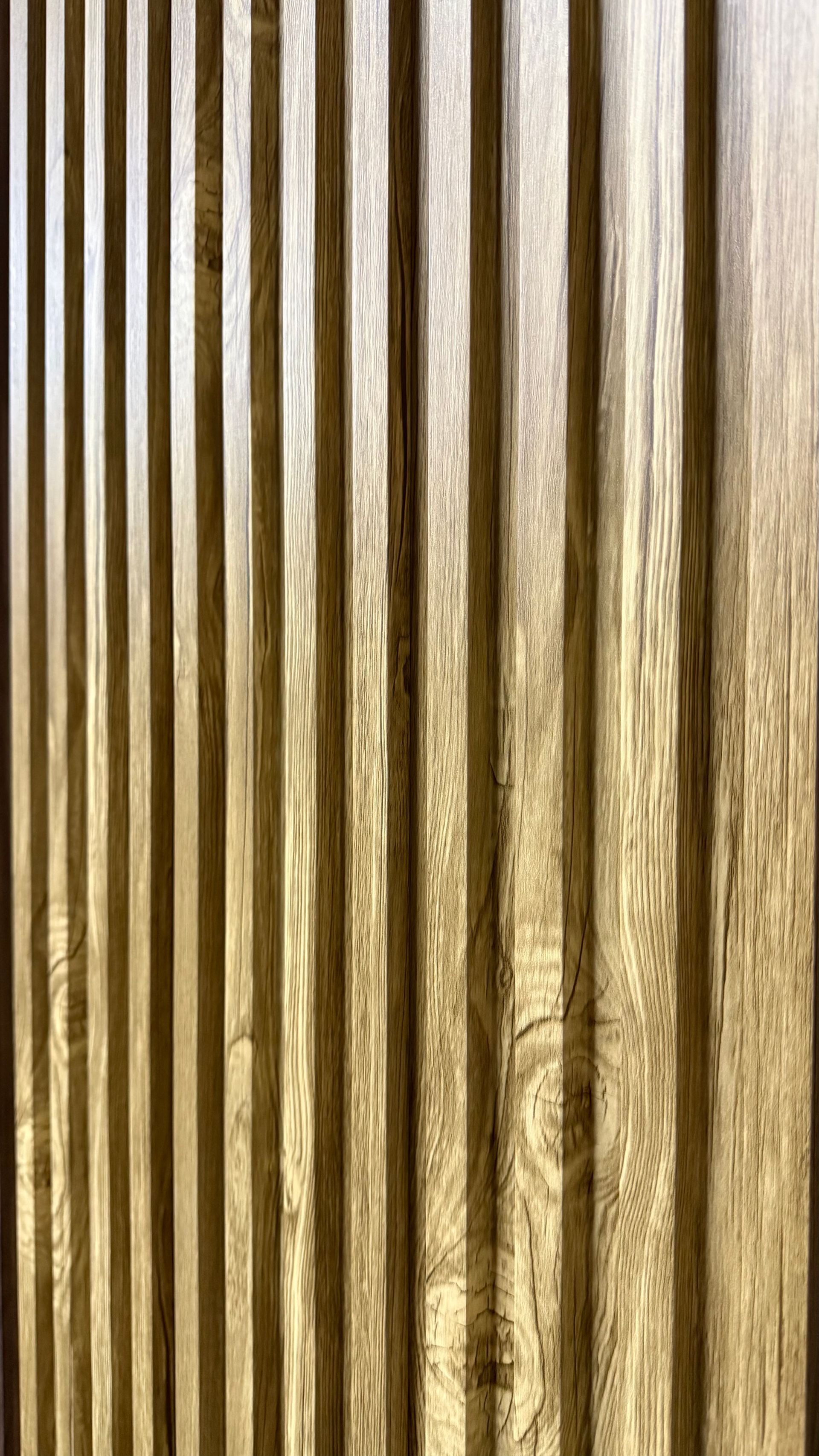Primer plano vertical de estrechas lamas de madera marrón con la luz reflejándose entre ellas.