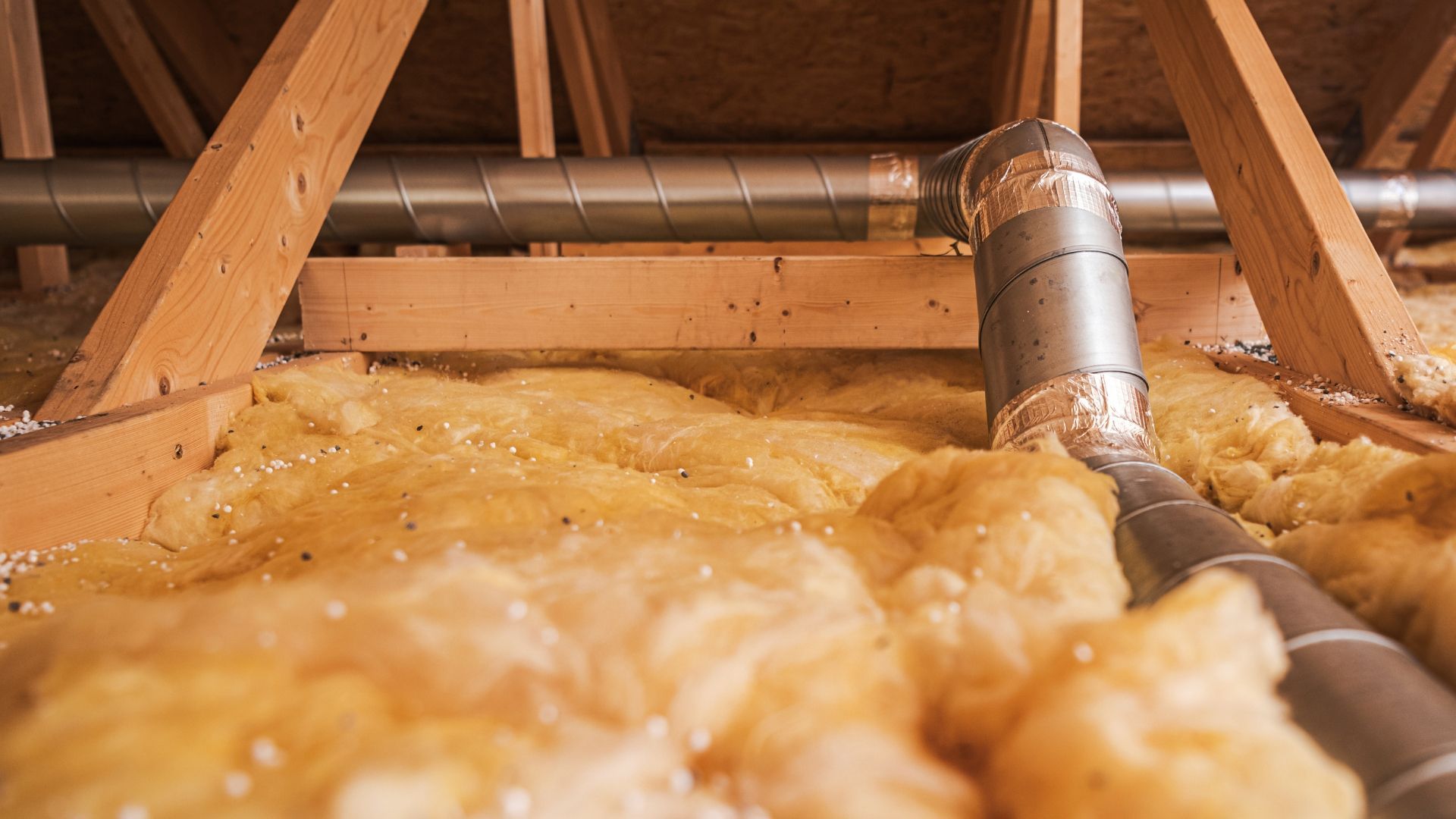 Attic with exposed wooden rafters, metal ducting, and yellow insulation batts