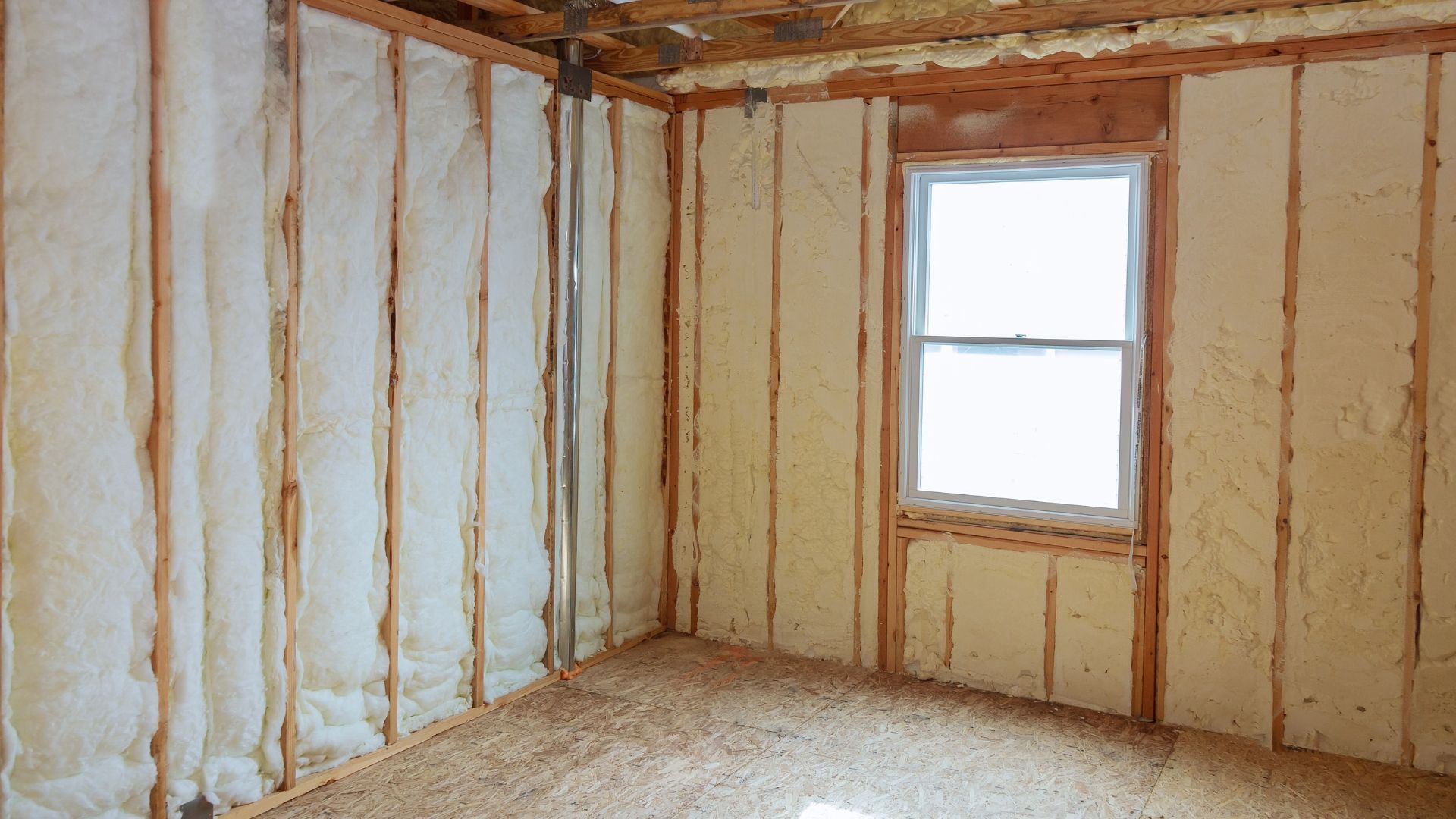 Empty unfinished room with exposed insulation, beige walls, and a single window.