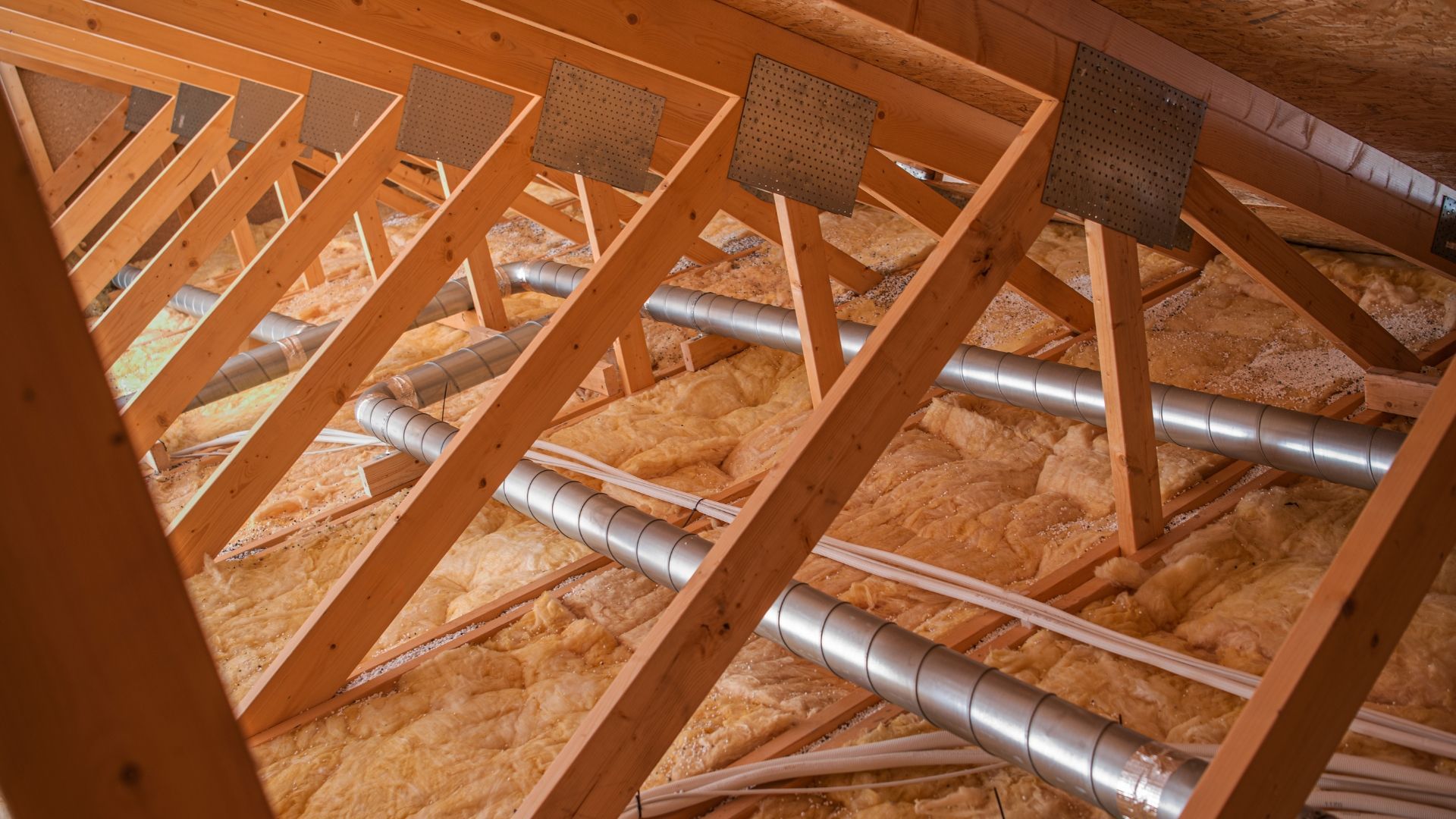Attic framing with wooden trusses, insulation, and silver HVAC ducts