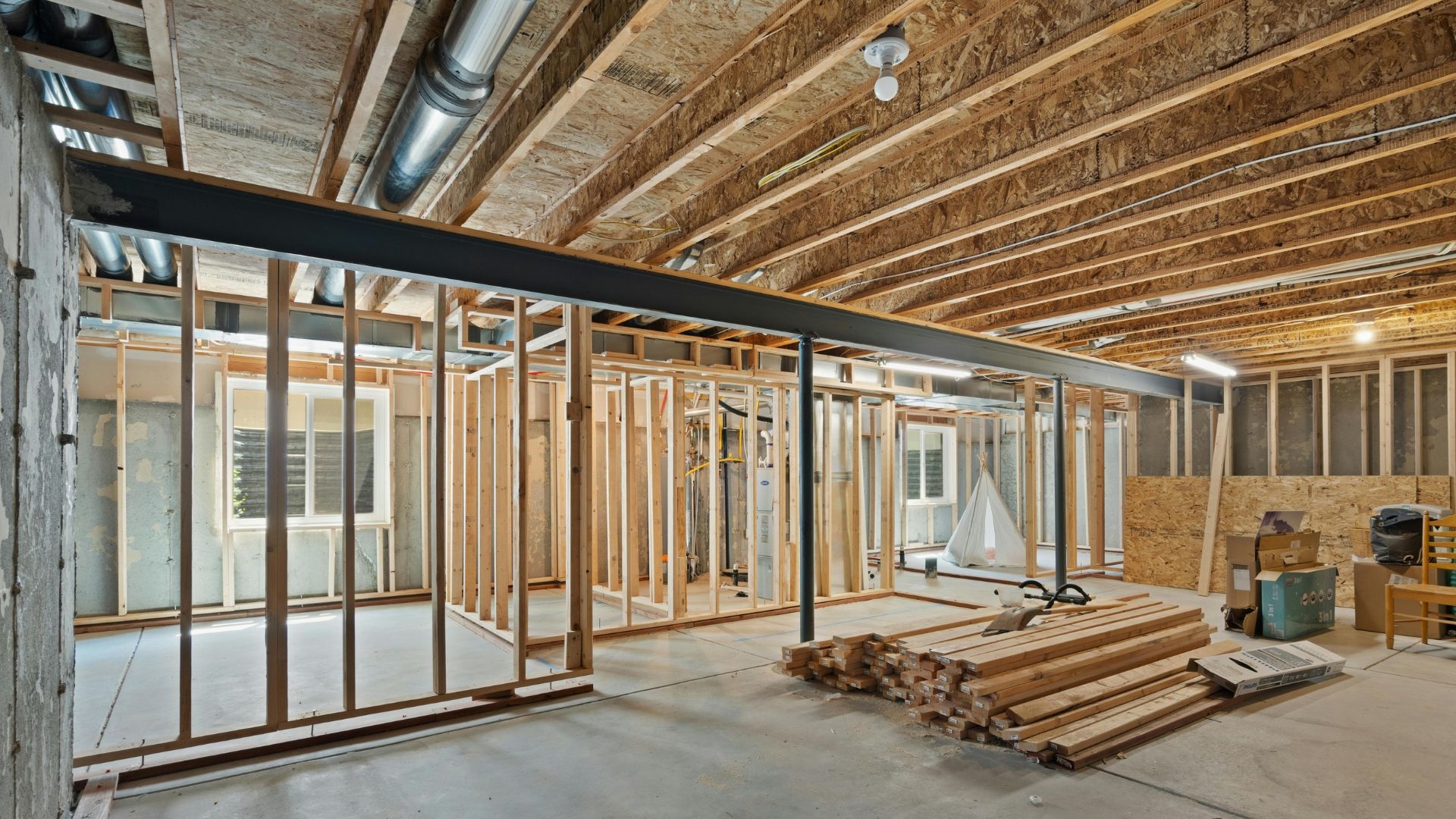 Interior of a house under construction with exposed framing, insulation, stacked lumber, and unfinished ceiling joists