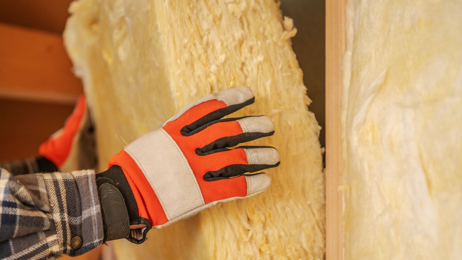 Gloved hand pressing yellow insulation batts between wall studs