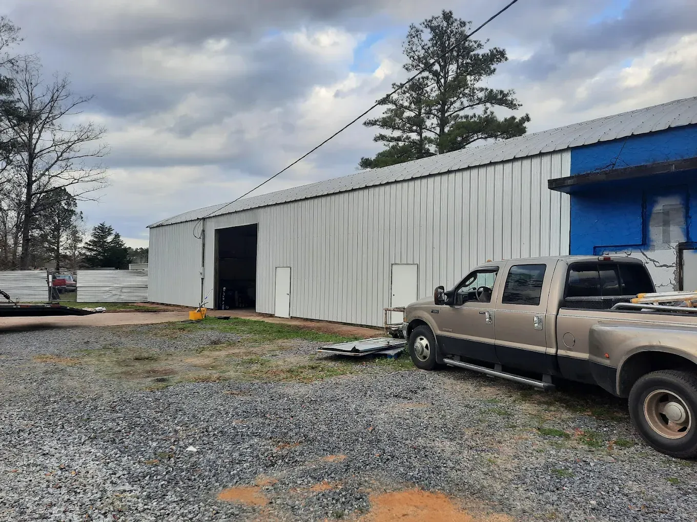 White metal warehouse with open door and parked pickup truck on a gravel lot under cloudy sky