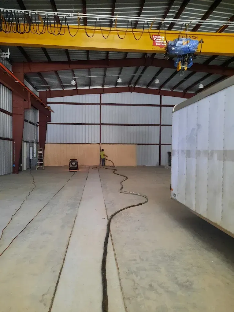 Industrial warehouse interior with overhead crane, concrete floor, and large white container on the right