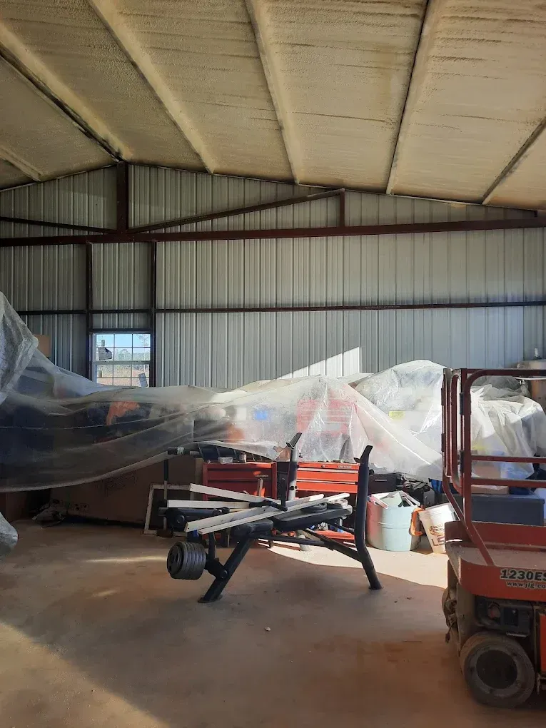 Large metal barn interior with covered machinery and a red forklift on the right