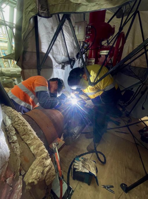 Two Men Are Welding A Pipe In A Room — Hanby Welding & Engineering In Portsmith, QLD