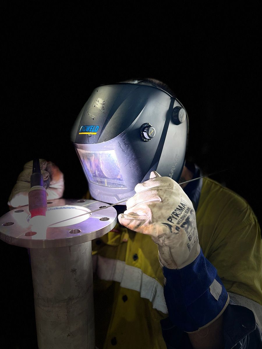 A Man Wearing A Welding Helmet And Gloves Is Welding A Pipe — Hanby Welding & Engineering In Portsmith, QLD