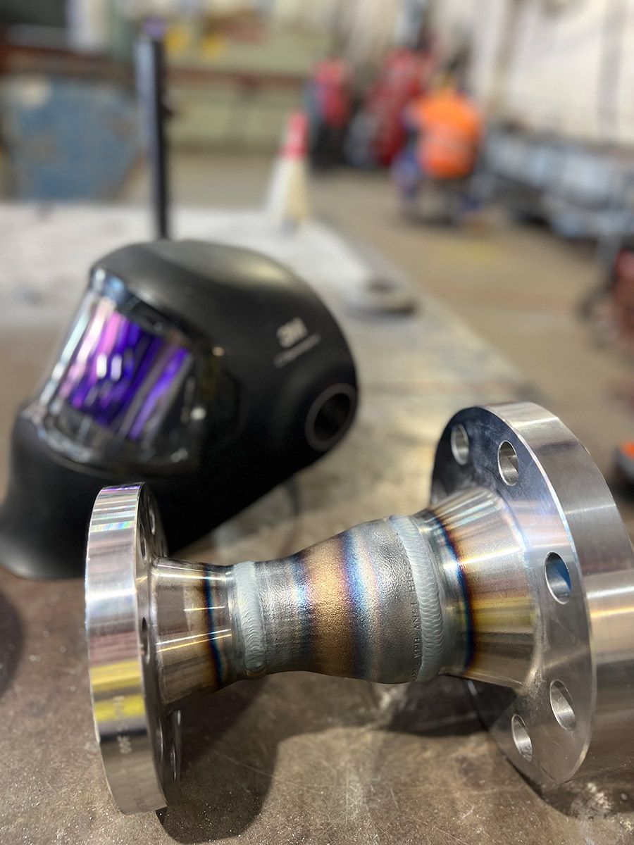 A Welding Helmet And A Piece Of Metal Are On A Table — Hanby Welding & Engineering In Portsmith, QLD