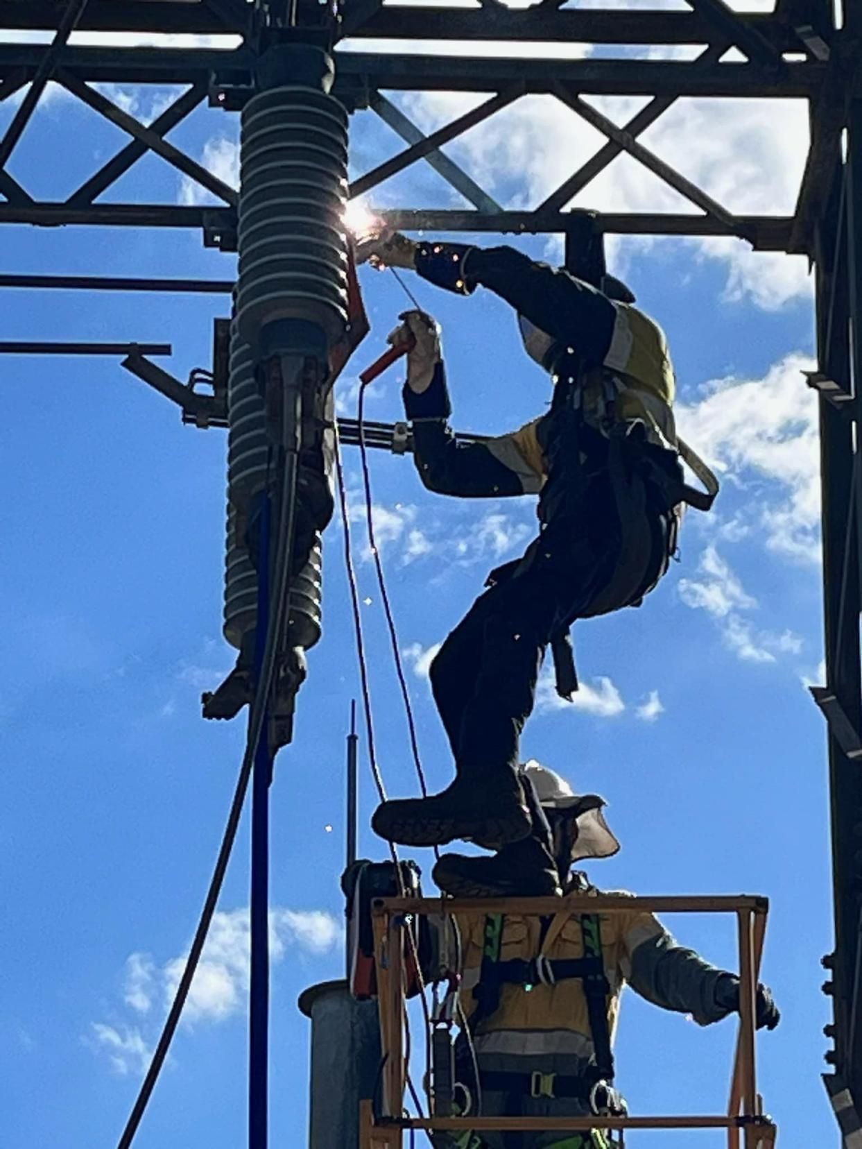 A Man Is Welding On A Power Line While Standing On A Platform — Hanby Welding & Engineering In Portsmith, QLD