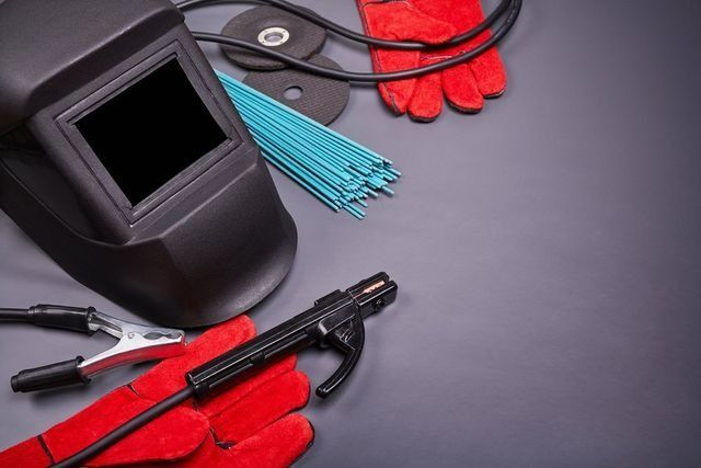 A Helmet, Gloves, Welding Rods, And Welding Supplies On A Table — Hanby Welding & Engineering In Portsmith, Qld