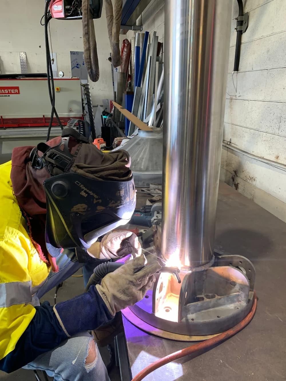 A Man Is Welding A Metal Pipe In A Garage — Hanby Welding & Engineering In Portsmith, QLD