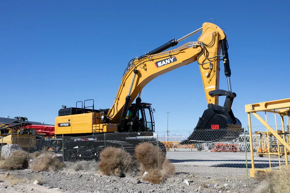 Yellow SANY excavator on a construction site, against a bright blue sky.