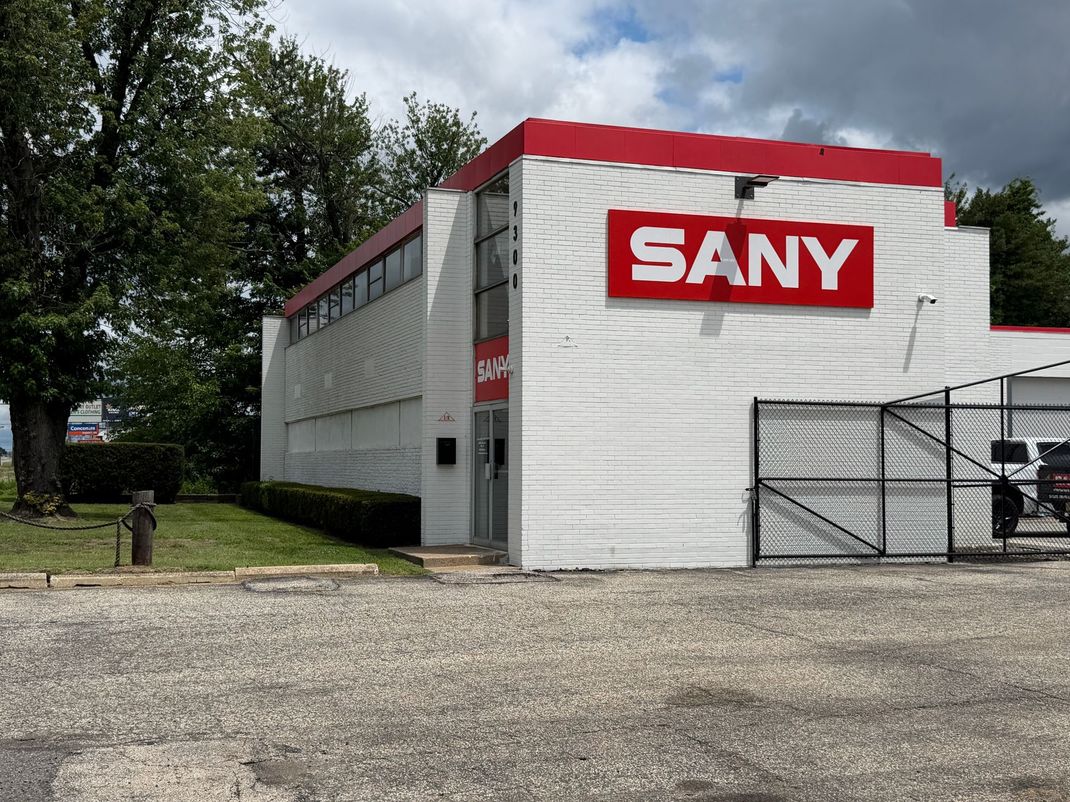 SANY building with red and white facade, black truck parked in front, blue sky.
