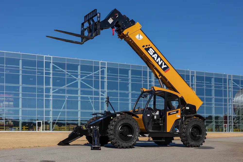 A yellow SANY telehandler with an extended boom and forks, parked in front of a modern glass building.
