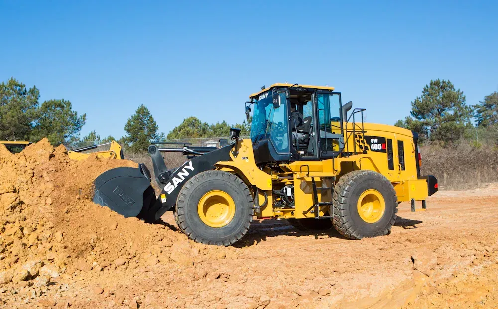Yellow SANY wheel loader digging in dirt on a sunny day.