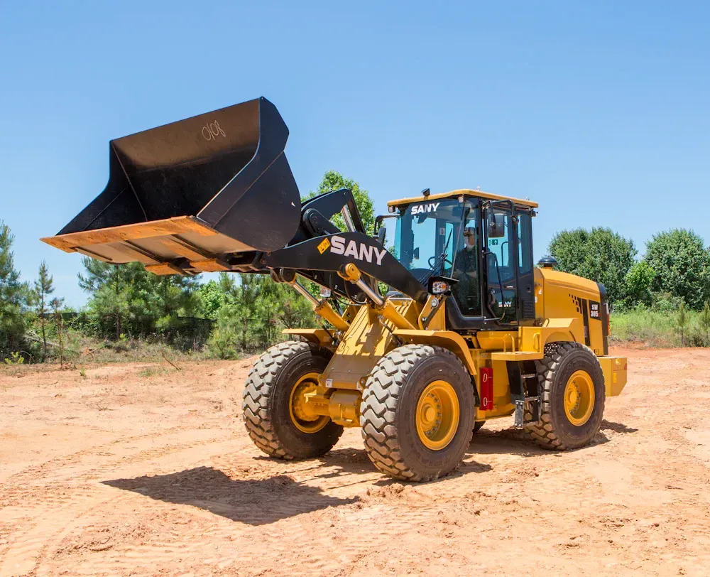 A yellow Sany wheel loader with a large raised bucket sits on a dirt construction site under a clear blue sky.