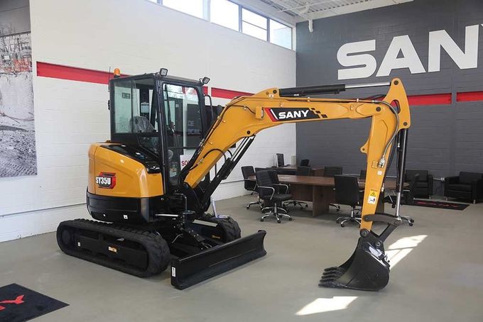 Yellow SANY excavator on green grass in front of a building.
