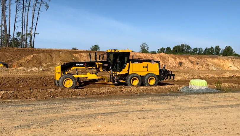 Yellow motor grader on a dirt road, leveling soil on a construction site.