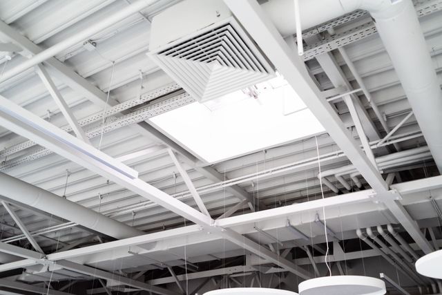 White industrial ceiling with exposed beams, ducts, and bright skylights