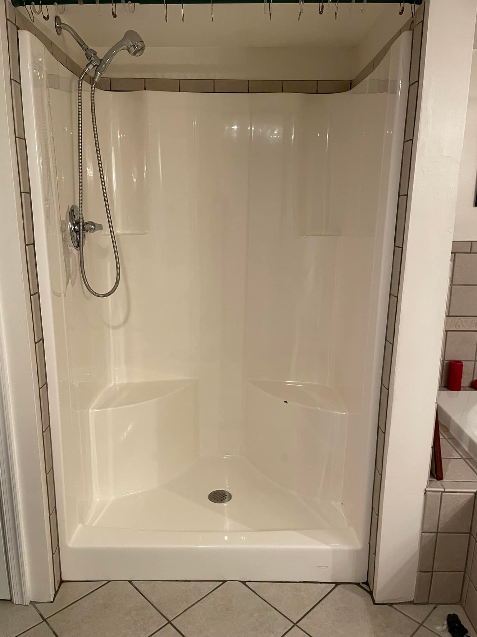 A white shower stall with two built-in seats and a shower head, flanked by white walls with decorative trim.