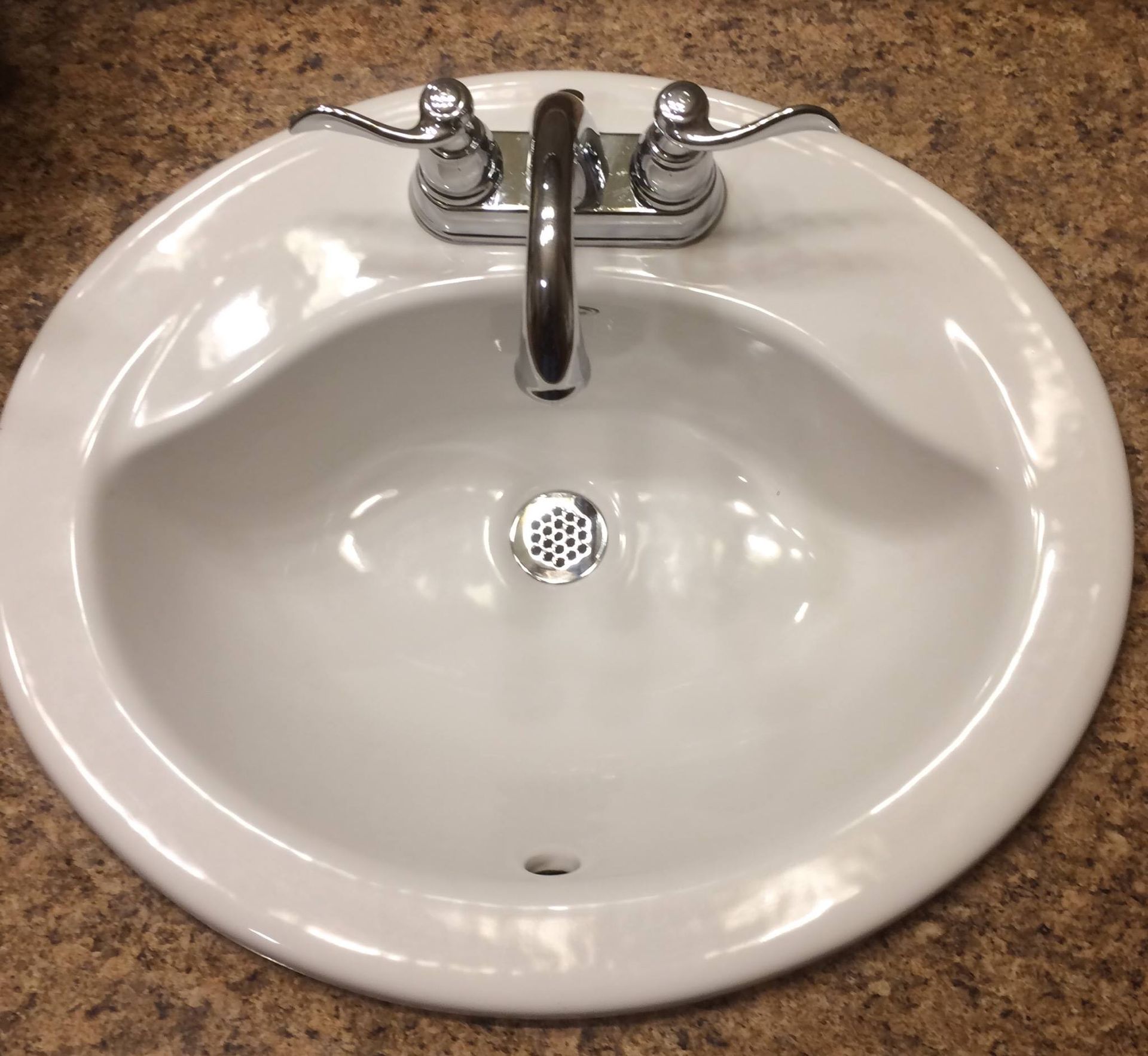 White, oval bathroom sink with chrome faucet and handles, set into a brown countertop.