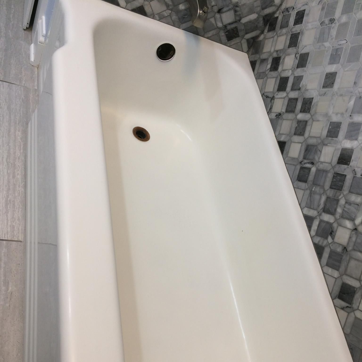 White bathtub with a black drain and overflow, set against a gray and blue mosaic tiled wall.