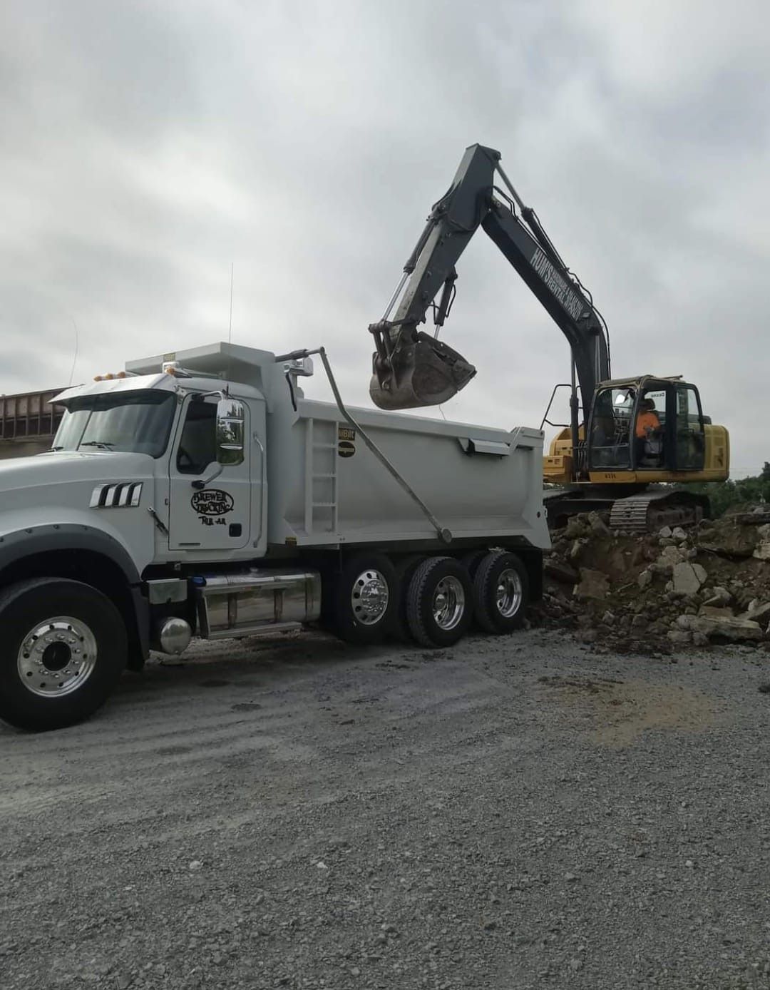A dump truck is being loaded with dirt by an excavator.