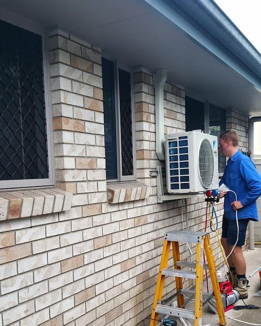 A Man Is Standing On A Ladder In Front Of A Brick Building — Coolmech In Noosa, QLD