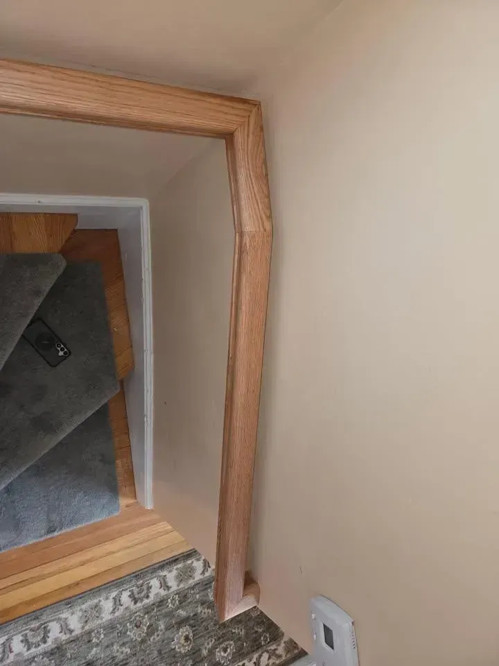 Wooden stair railing beside a carpeted staircase and hallway corner with white walls