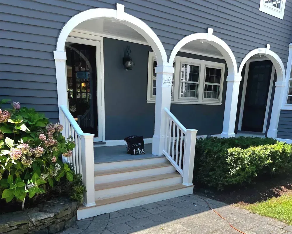 Blue house entrance with white arches, steps, and a black cat on the front porch