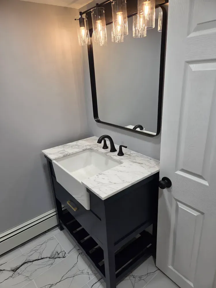 Modern bathroom vanity with marble countertop, black fixtures, mirror, and wall sconce lighting