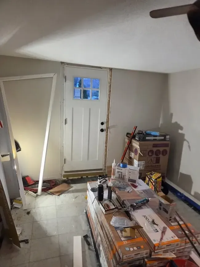 Cluttered room with stacked boxes, tools, and a white door under a sloped ceiling.