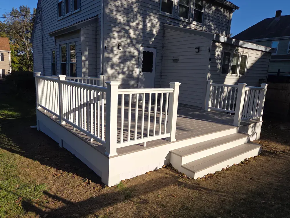 White-railed front porch with steps on a gray house in a yard