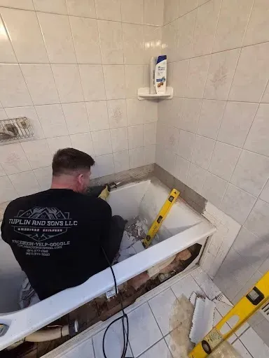 Worker installing a bathtub in a tiled bathroom, with tools and level guides visible