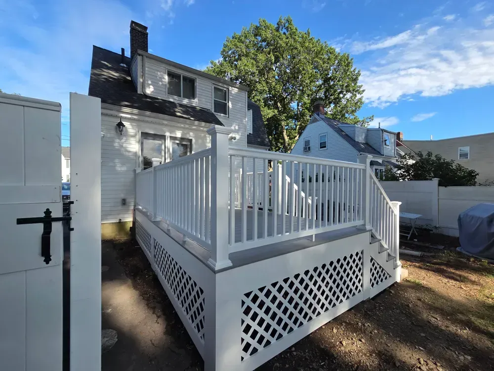 White raised deck with lattice skirting beside a gray house under a blue sky