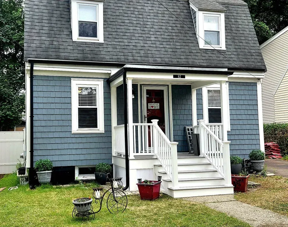 Small blue house with white trim and porch steps, front yard, and dormer windows.