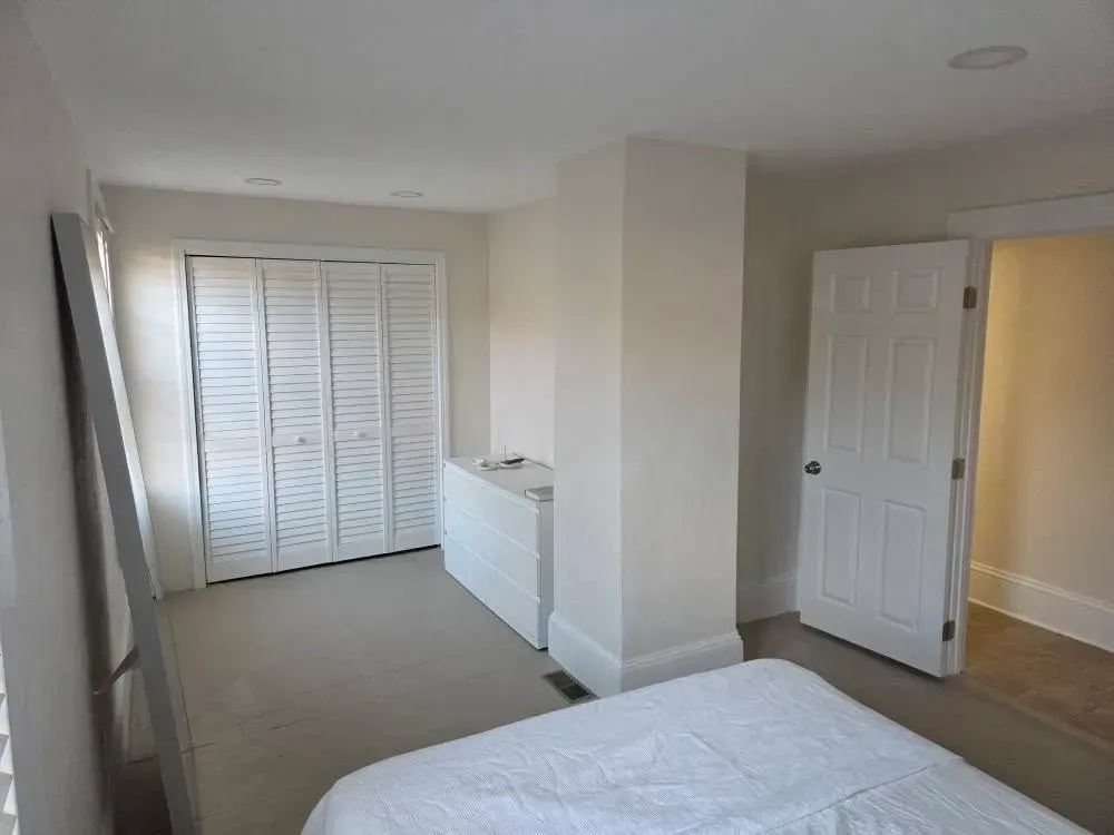 Empty beige bedroom with bed, closet doors, and open doorway to hall