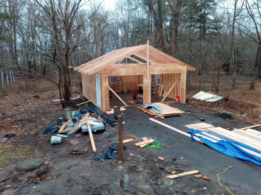 Partially built wooden cabin with exposed framing and construction materials scattered on a muddy lot