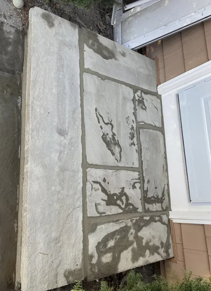 Weathered concrete wall or slab with cracked patches beside a house exterior.