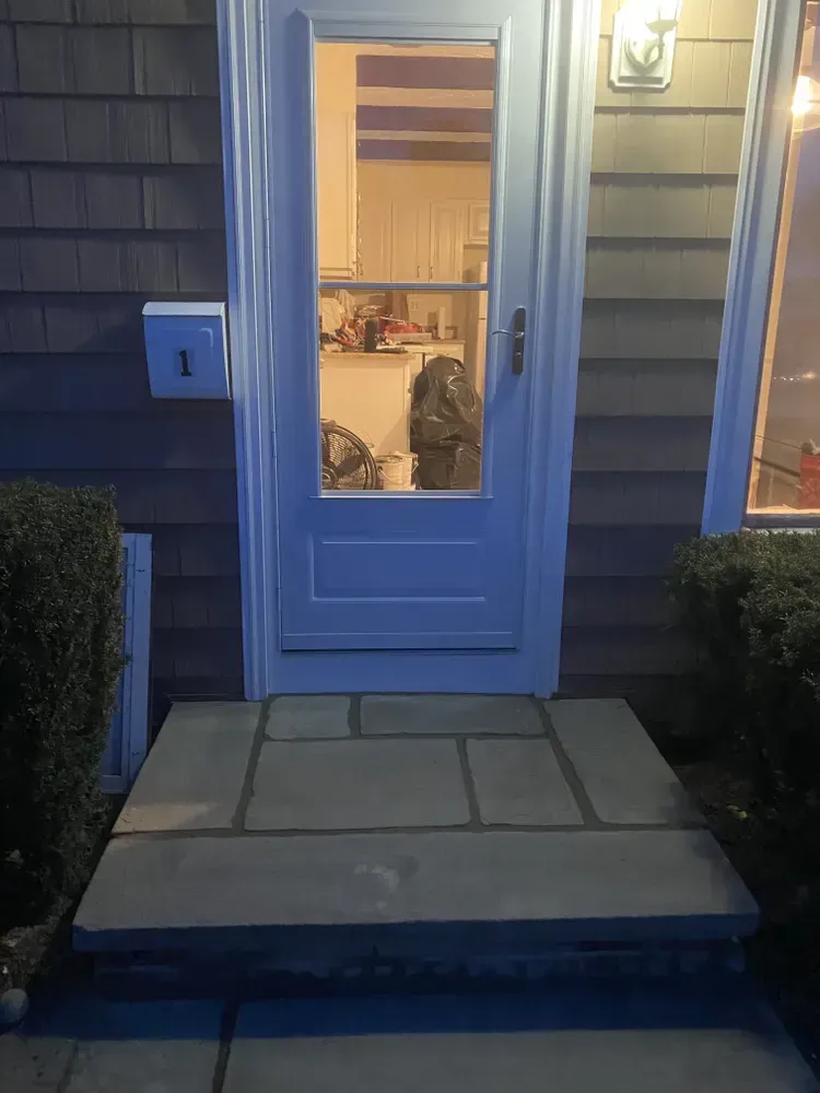 Front door with glass panel and lit porch steps at dusk, with a cat visible inside near the window.