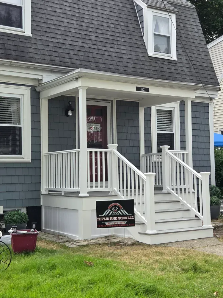 Gray house with white porch and steps, small sign in front, and manicured lawn.
