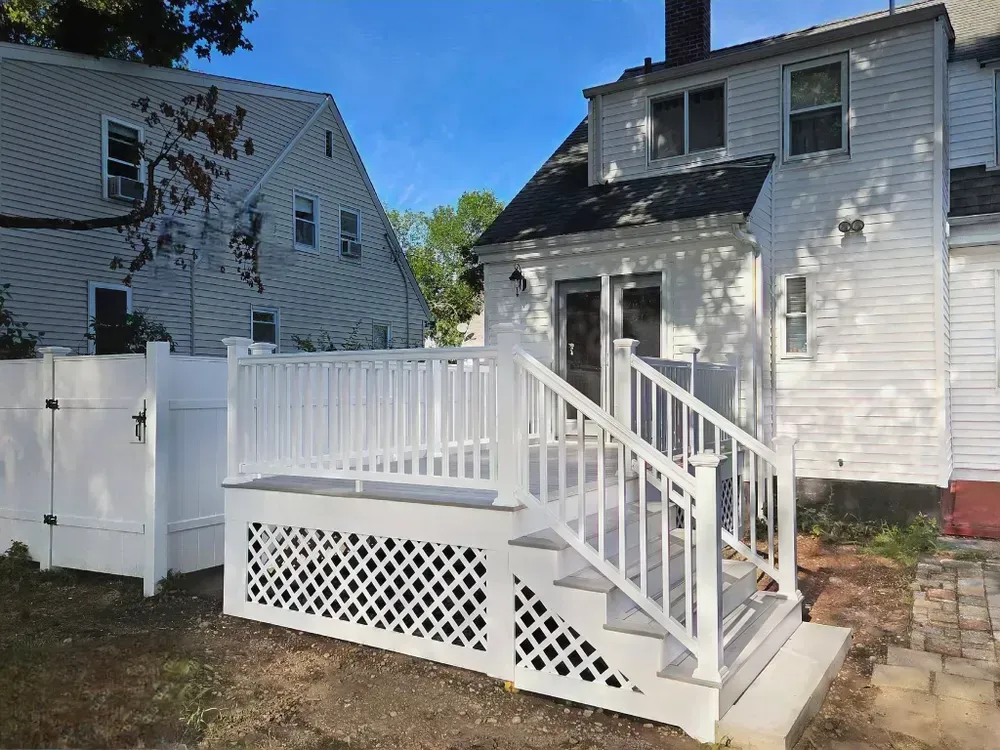 White raised deck with stairs and lattice under a gray house in a sunny yard