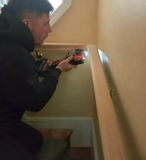 Person crouches on stairs, using a handheld thermal camera to inspect a wall.