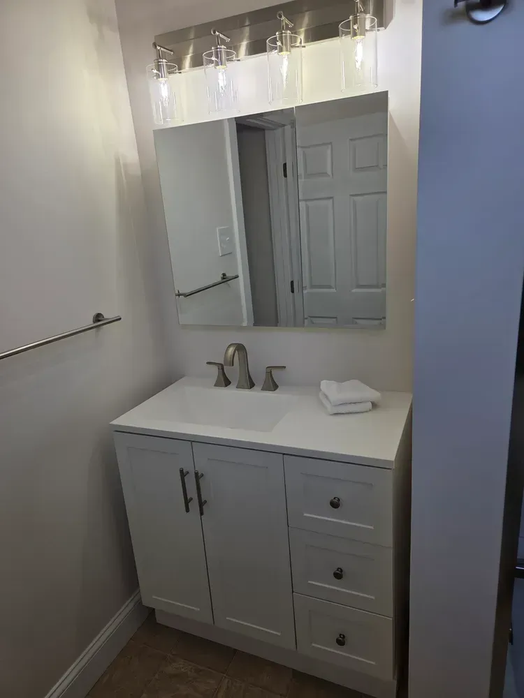 Small bathroom vanity with white cabinet, mirror, sink, and towel on the counter.