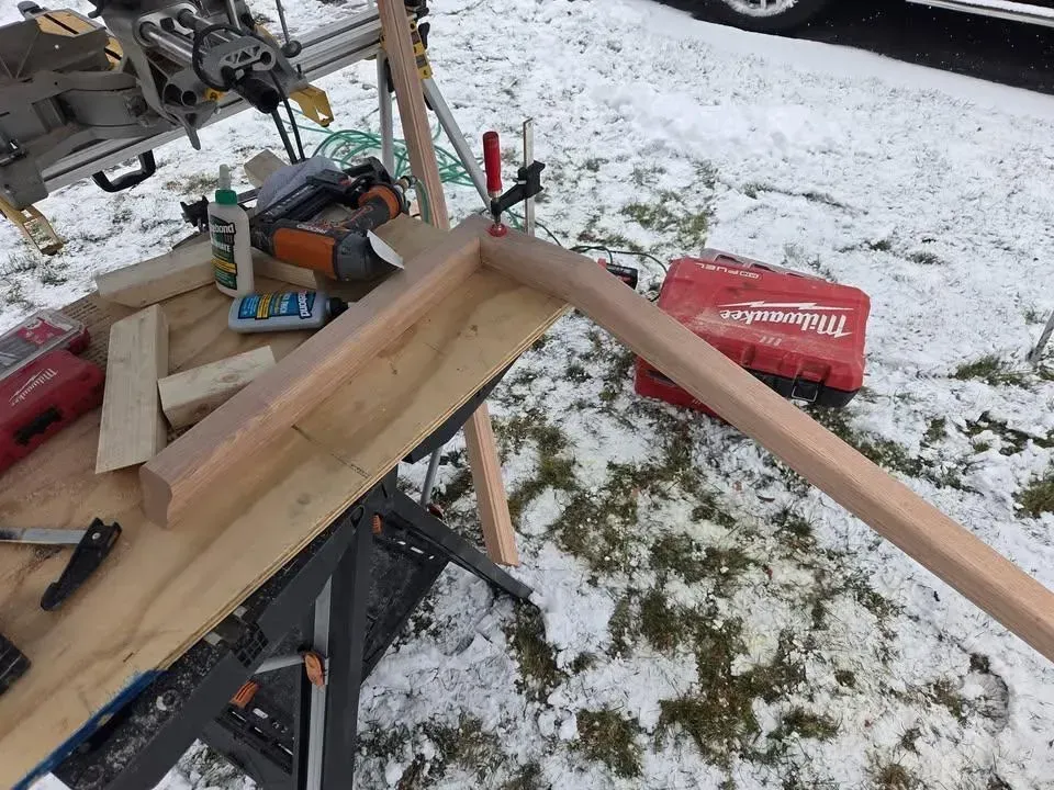 Workshop workbench with lumber, clamps, and tools beside a snowy yard