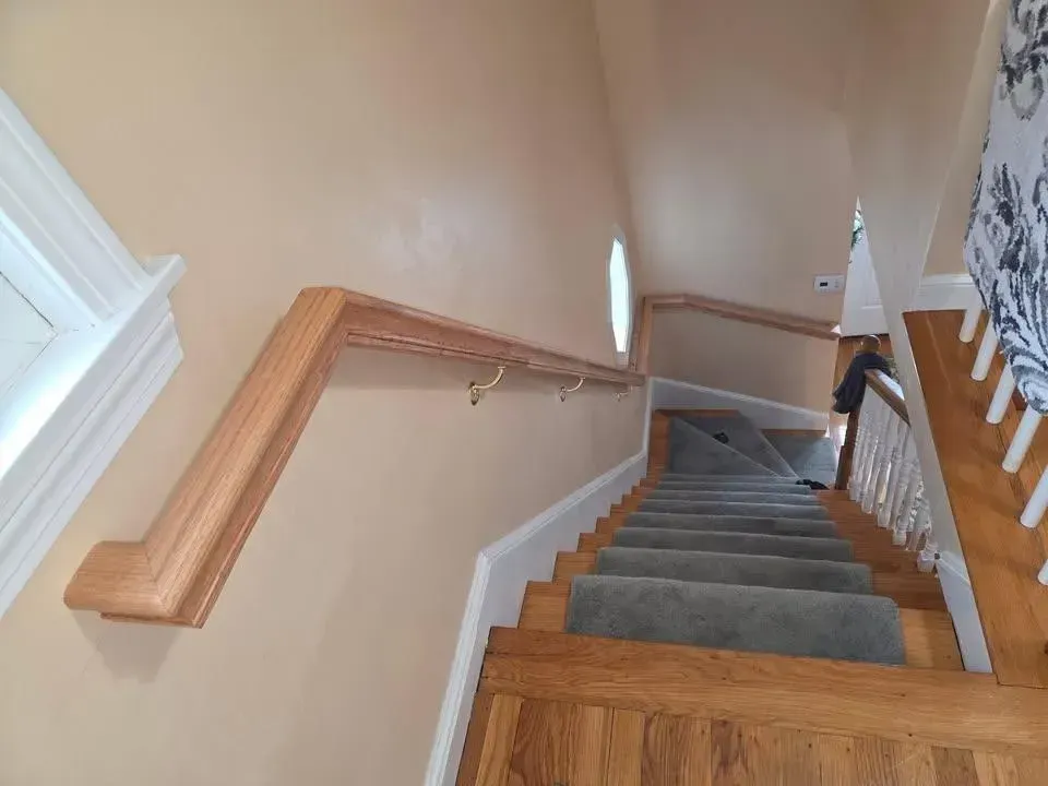 Wooden staircase with gray carpet runner, beige walls, and a handrail in a home interior