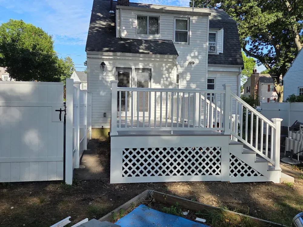 White house exterior with a raised deck, stairs, lattice skirting, and a fenced yard in daylight