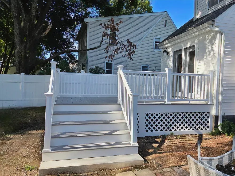 Front porch with white stairs, railing, and lattice on a house beside a fenced yard.